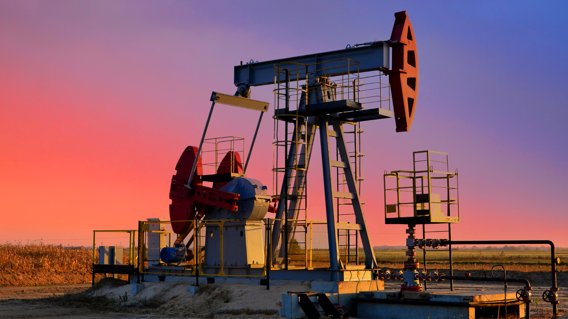 A classic oil pumpjack (nodding donkey) silhouetted against a dramatic red and purple sunset.