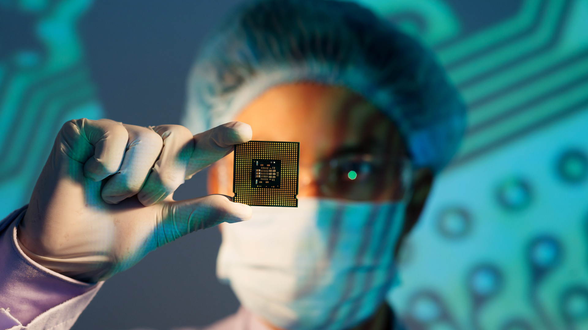 A technician in protective gear holding up a microchip (CPU or processor) for inspection.