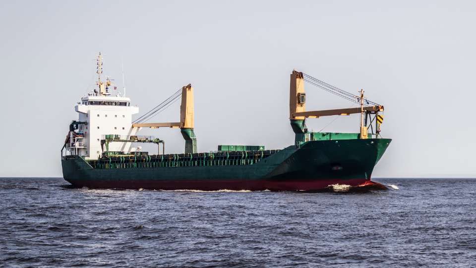 Medium-sized general cargo ship sailing across open blue sea, representing global shipping and maritime trade.