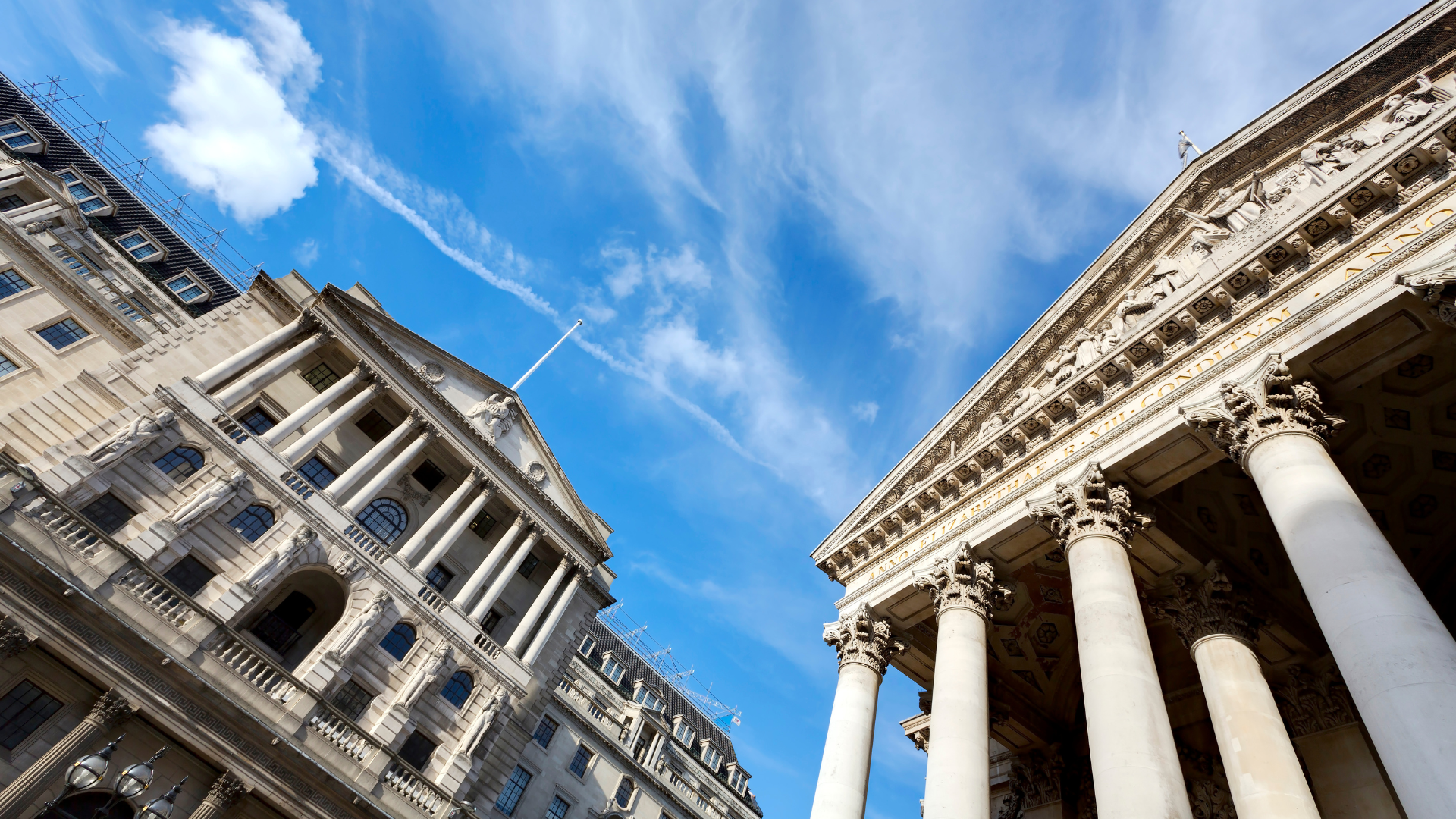 Historic neoclassical buildings of the Bank of England and the Royal Exchange under a bright blue London sky.