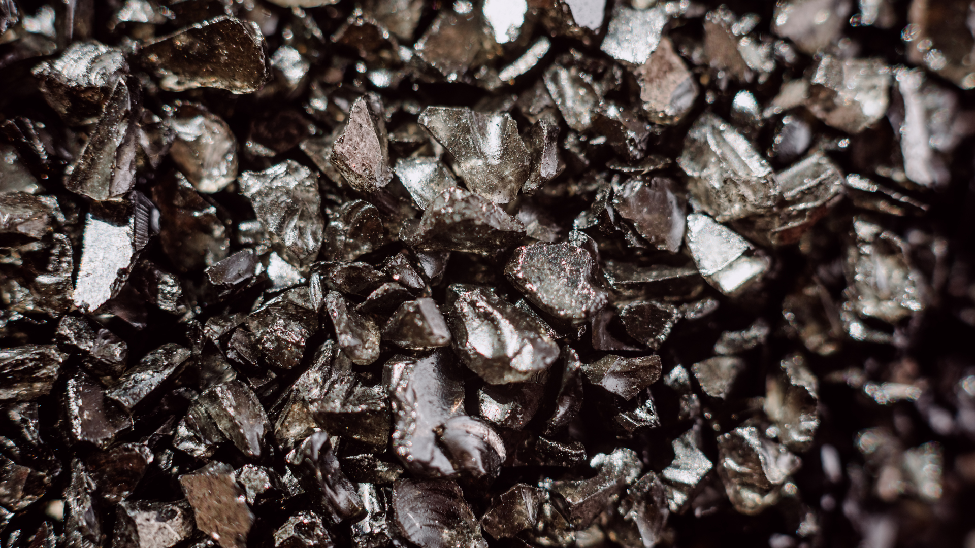 Extreme close-up of shiny black, angular crushed rock or granular material (e.g., obsidian, gravel).