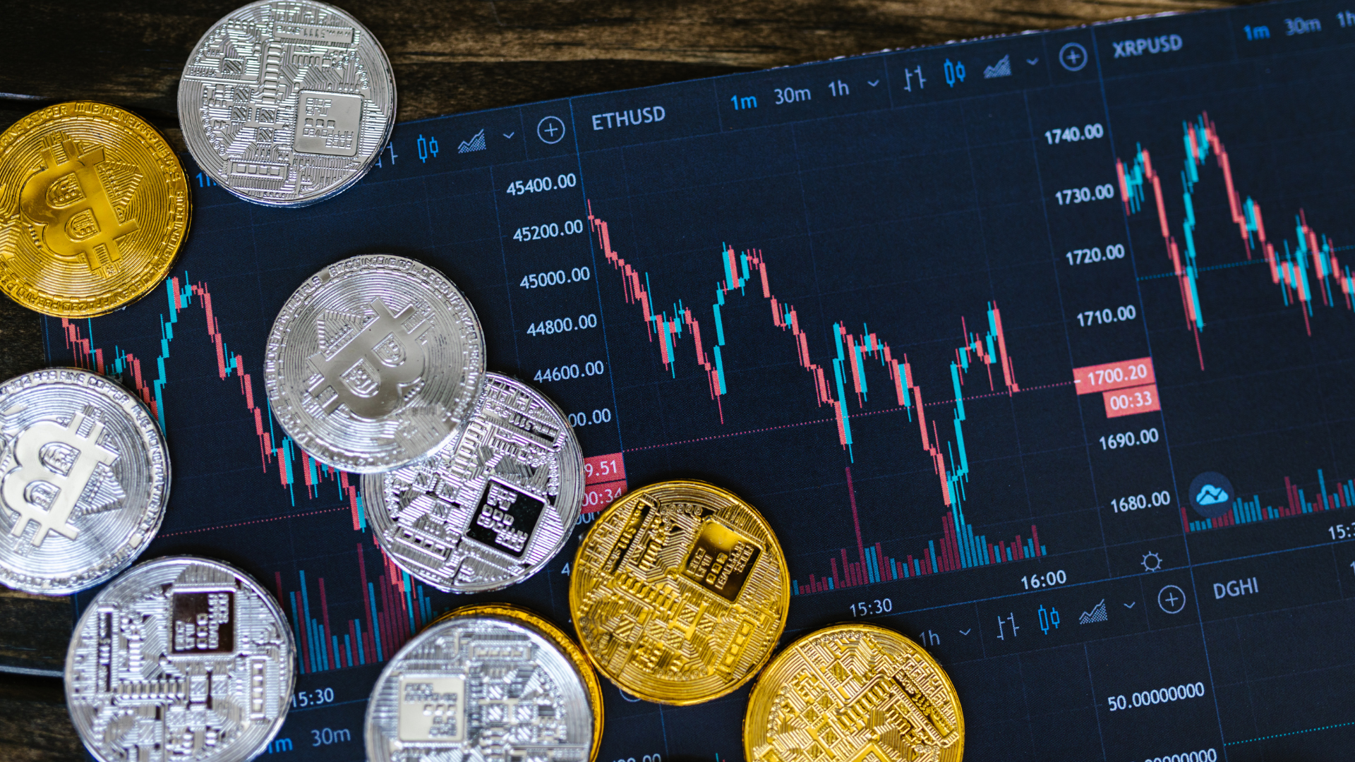 Physical Bitcoin and cryptocurrency coins placed on top of a digital trading chart showing crypto market price movements