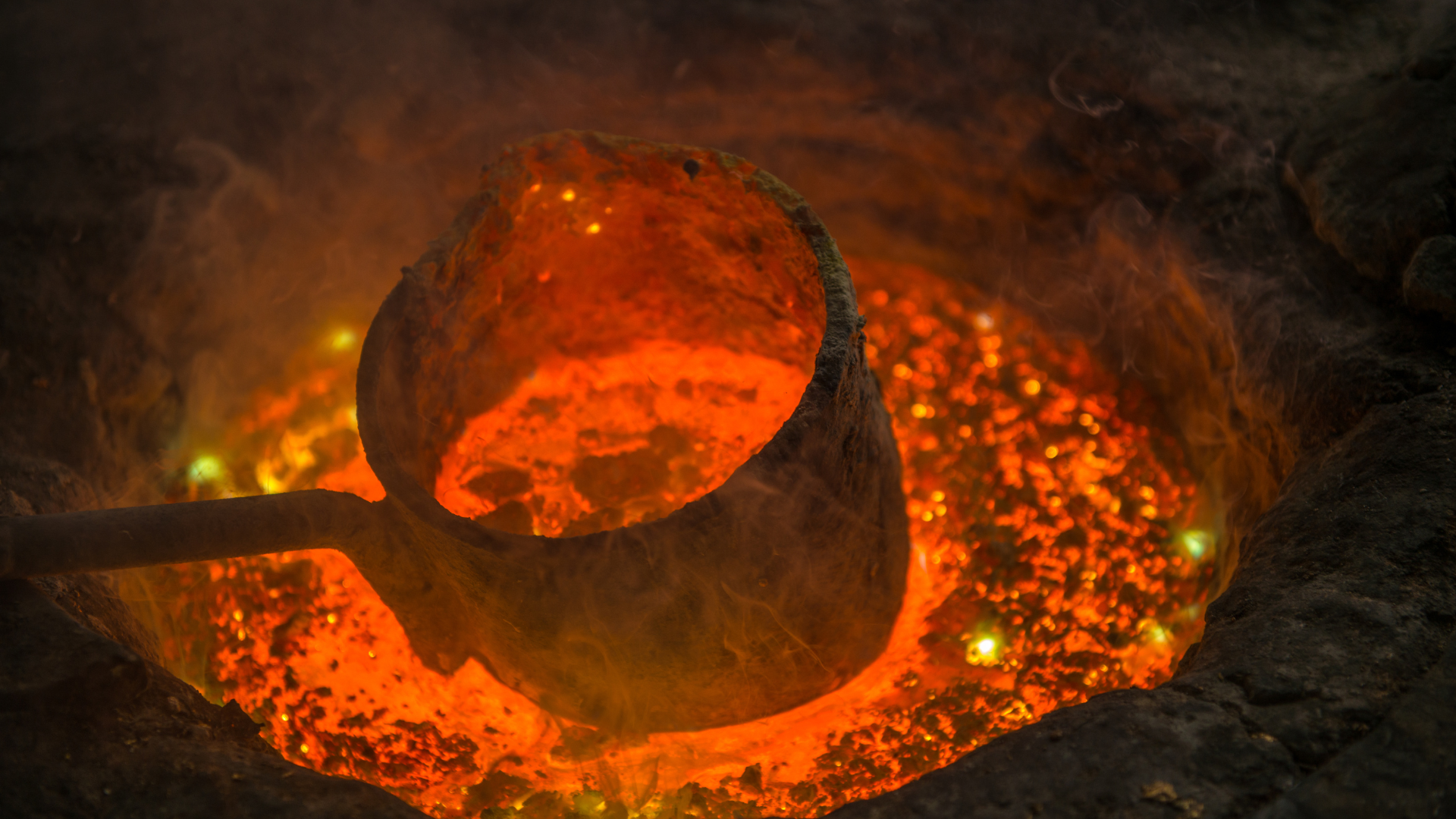 Molten metal glowing inside a furnace with a ladle positioned over the liquid metal.