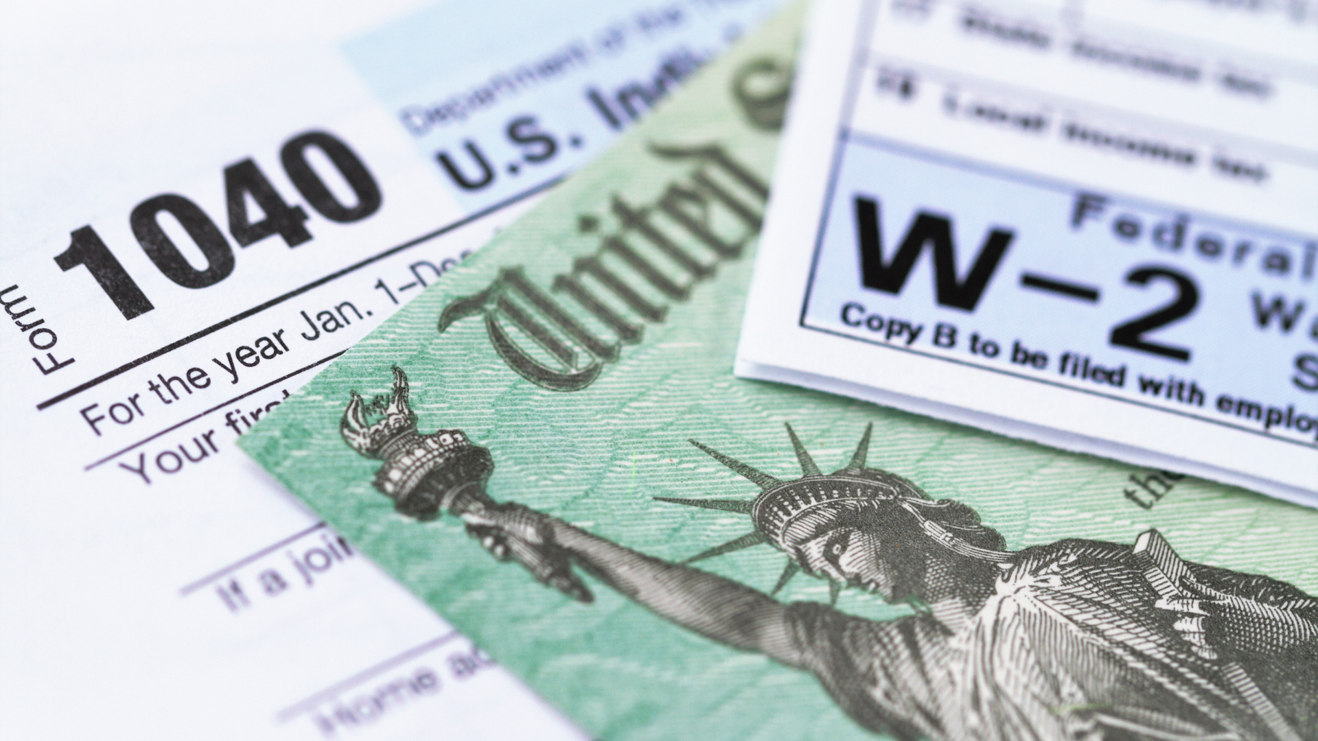Close-up of US tax forms (1040 and W-2) with a green dollar bill or tax rebate check showing the Statue of Liberty.