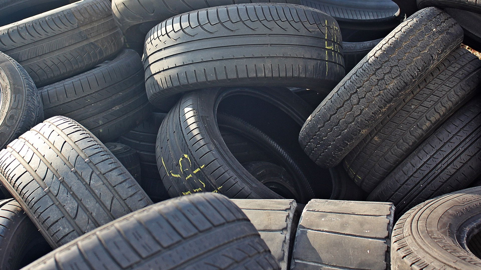 Large, messy pile of discarded, worn car tires at a recycling or storage facility.