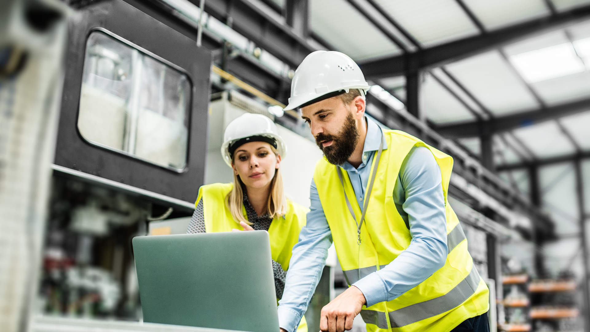 Engineers wearing safety vests and helmets reviewing data on a laptop in a factory.