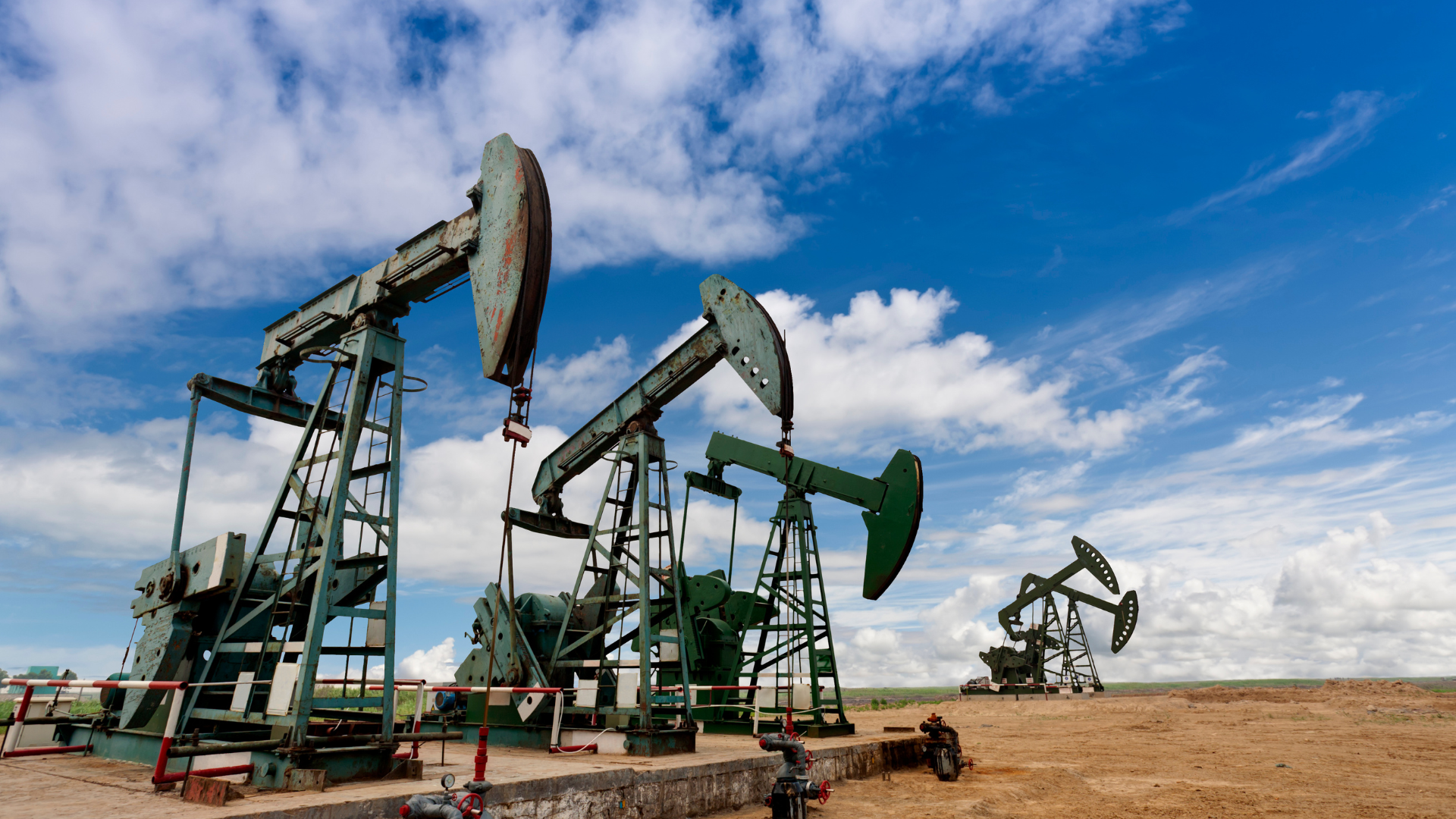 Oil pump jacks extracting crude oil from the ground under a blue sky.