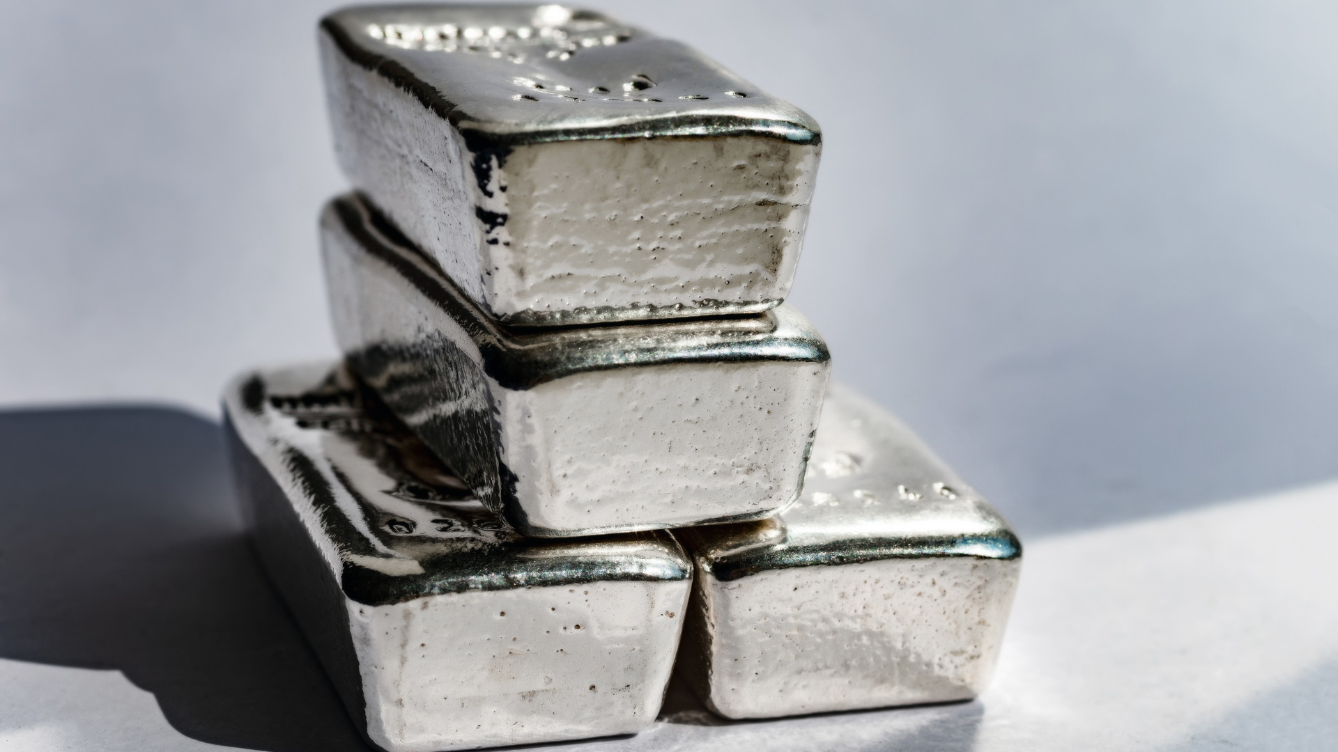 Stack of shiny silver bars reflecting light on a neutral background.