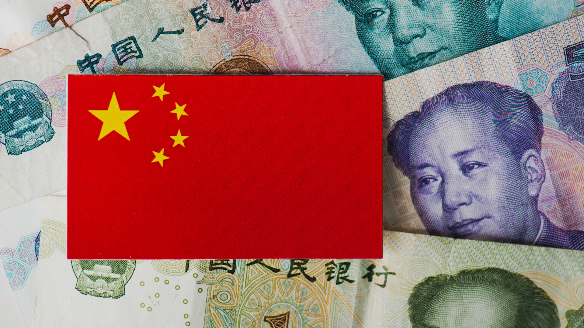 Chinese flag on top of yuan banknotes symbolizing China’s economy and currency.