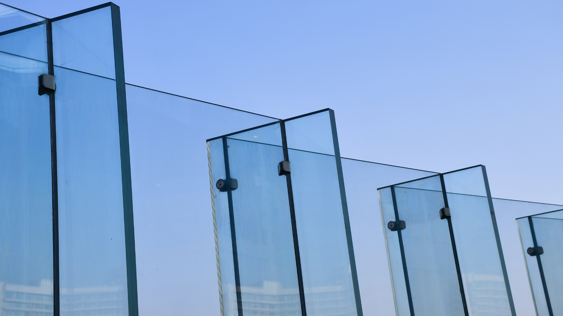 Modern glass railing panels with metal fittings against a clear blue sky.