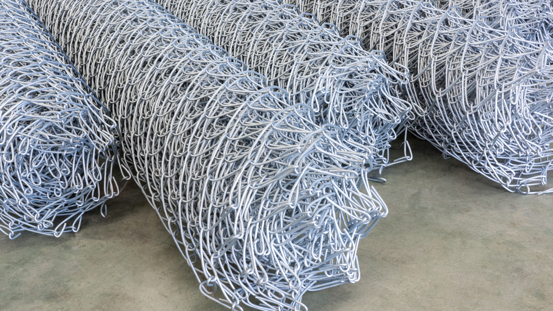 Rolls of galvanized steel wire mesh stacked on a concrete floor.