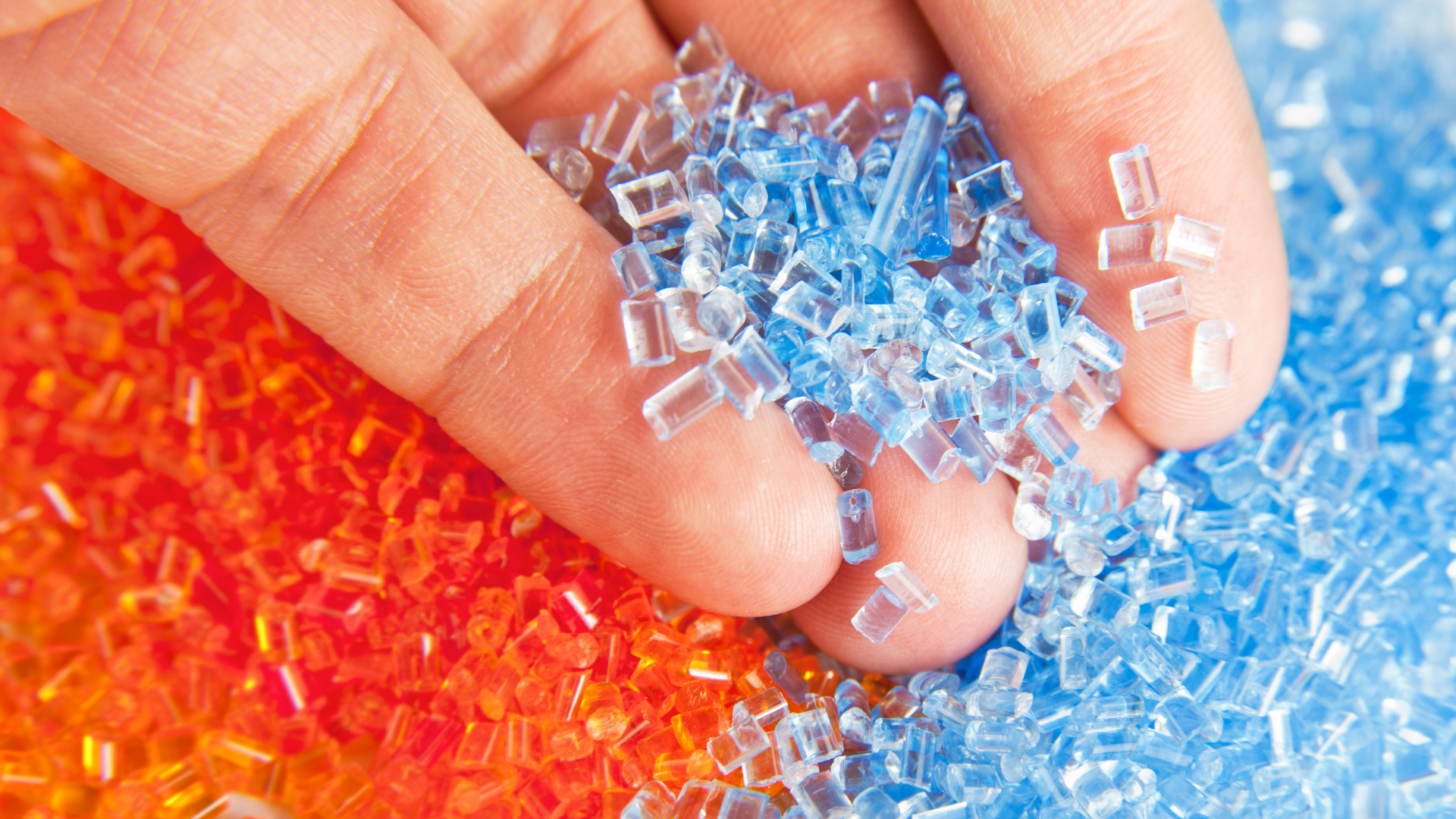 Hand holding blue and orange plastic polymer granules.
