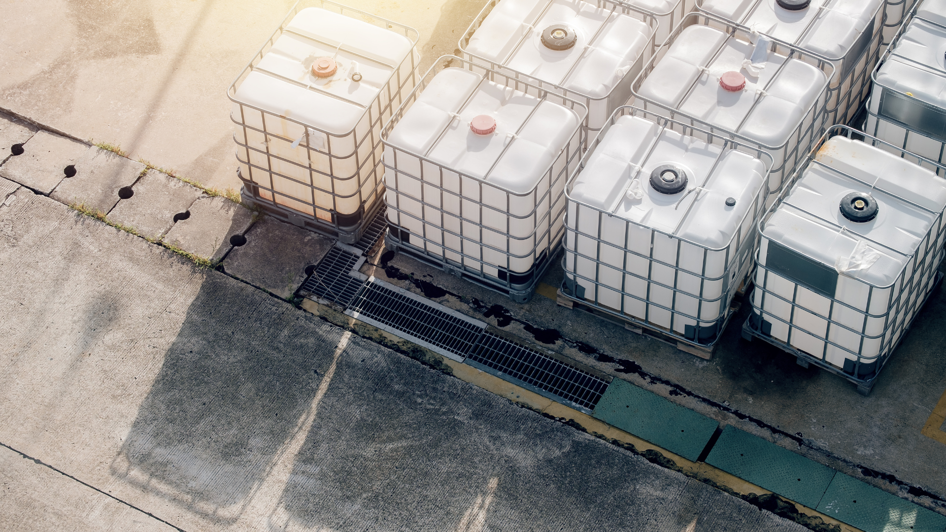 Large plastic IBC storage containers filled with industrial liquids placed outdoors on a concrete surface.