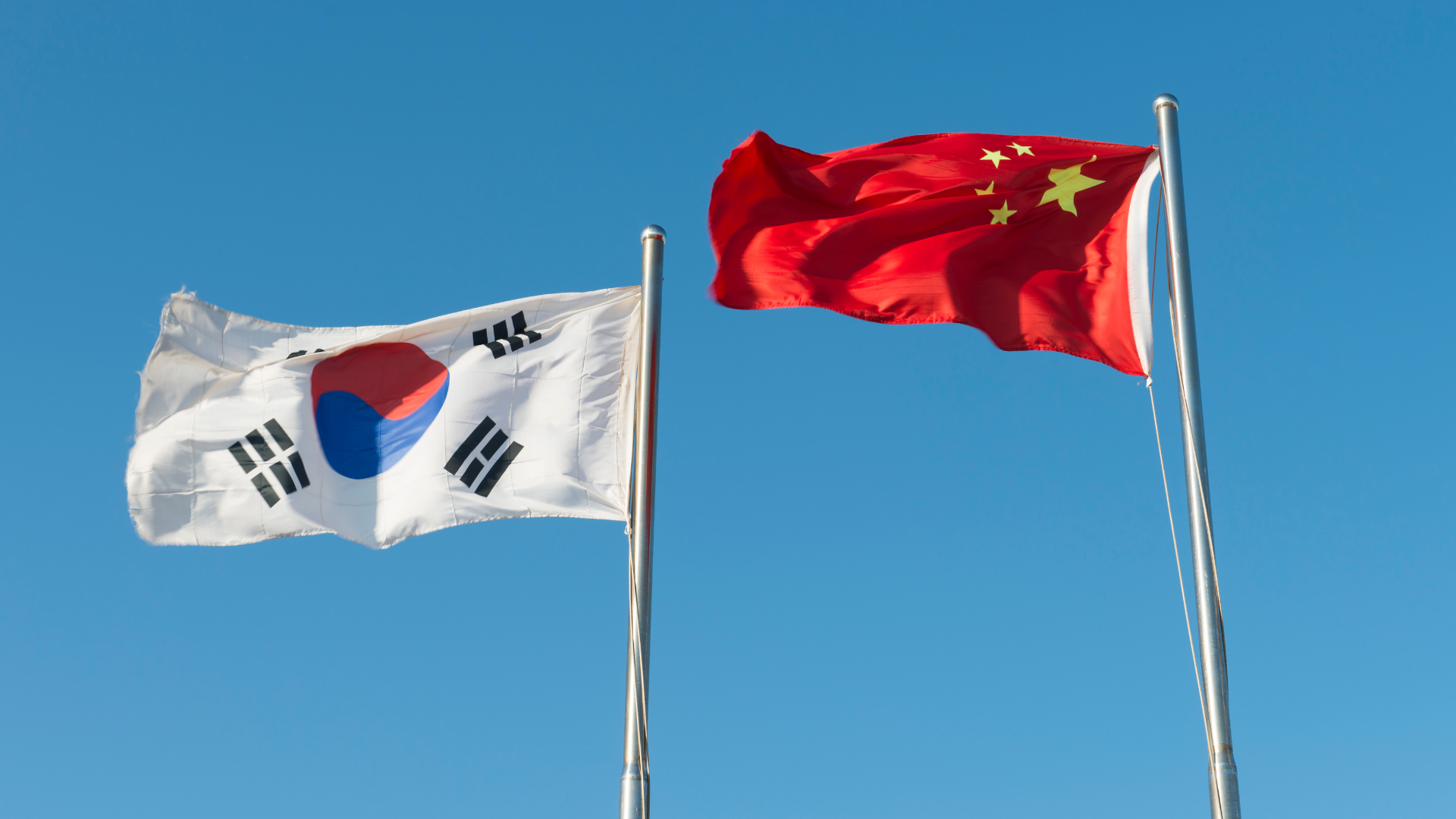 The national flags of South Korea and China flying side-by-side against a clear blue sky.