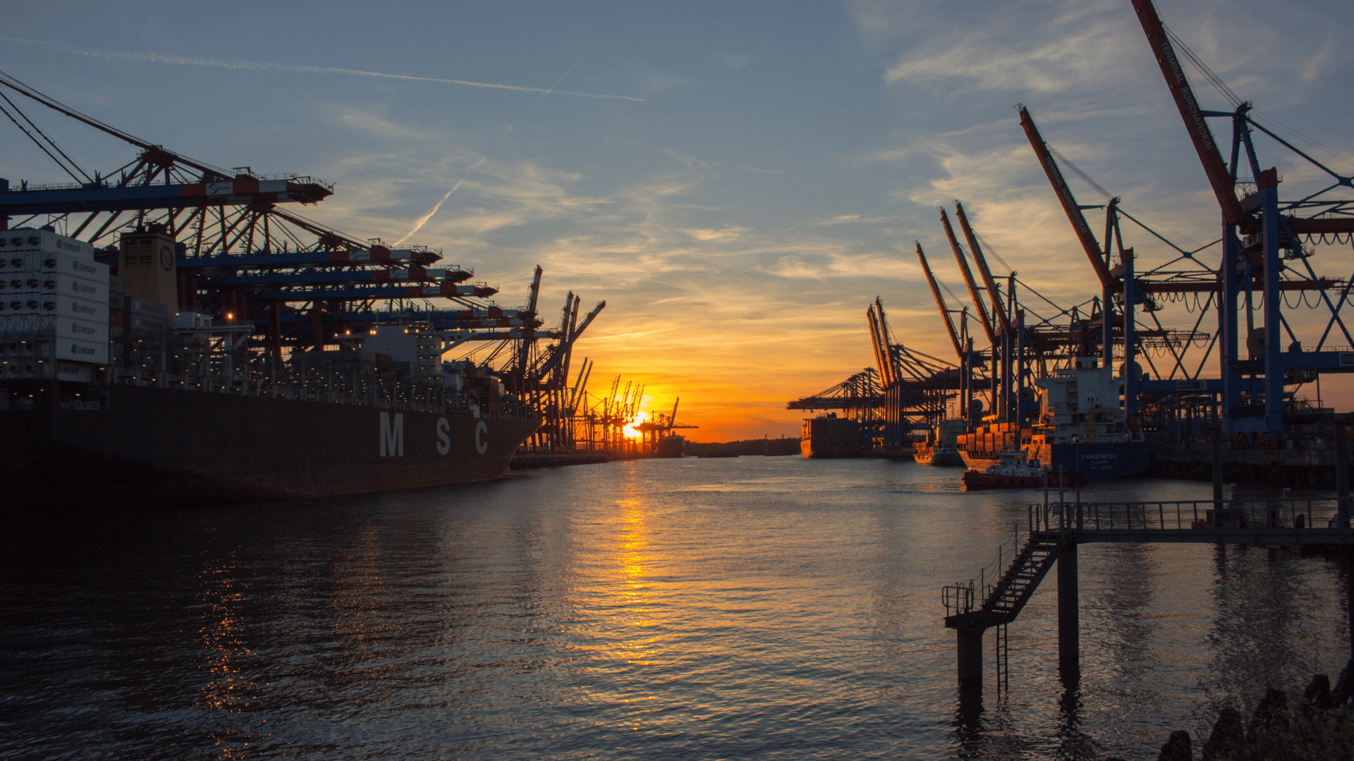 Cargo ships and cranes at a busy port during sunset.