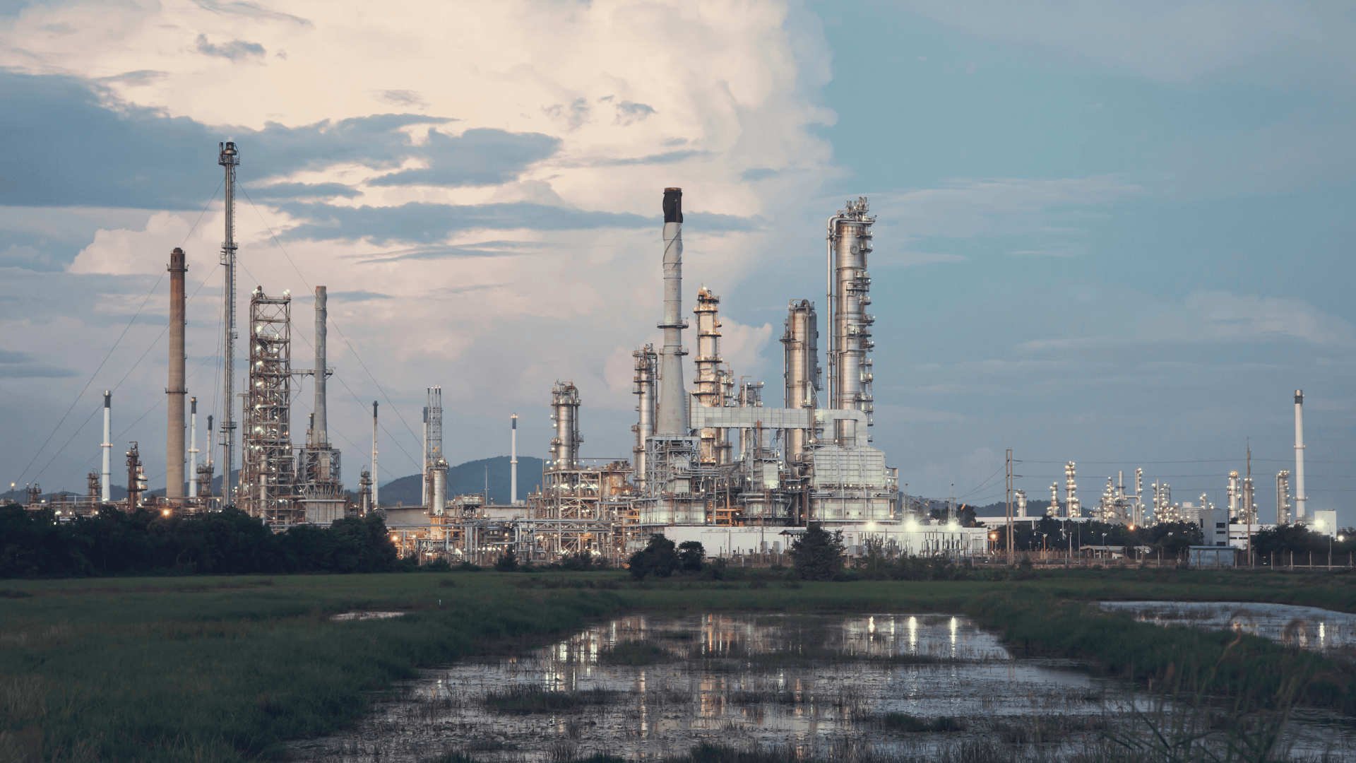 Industrial oil refinery with metal towers and pipelines under a cloudy sky.