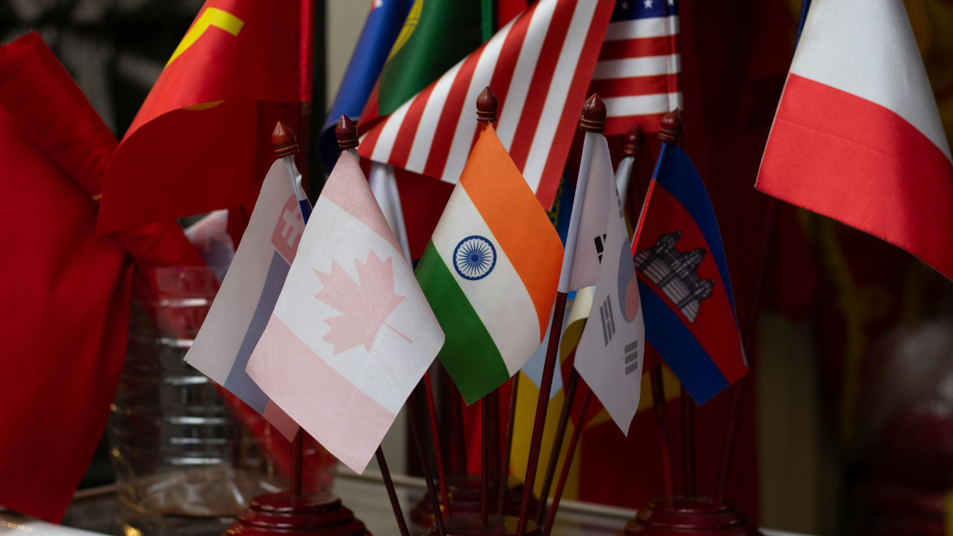 Cluster of miniature table flags representing multiple nations, including Canada, India, South Korea, and the USA.
