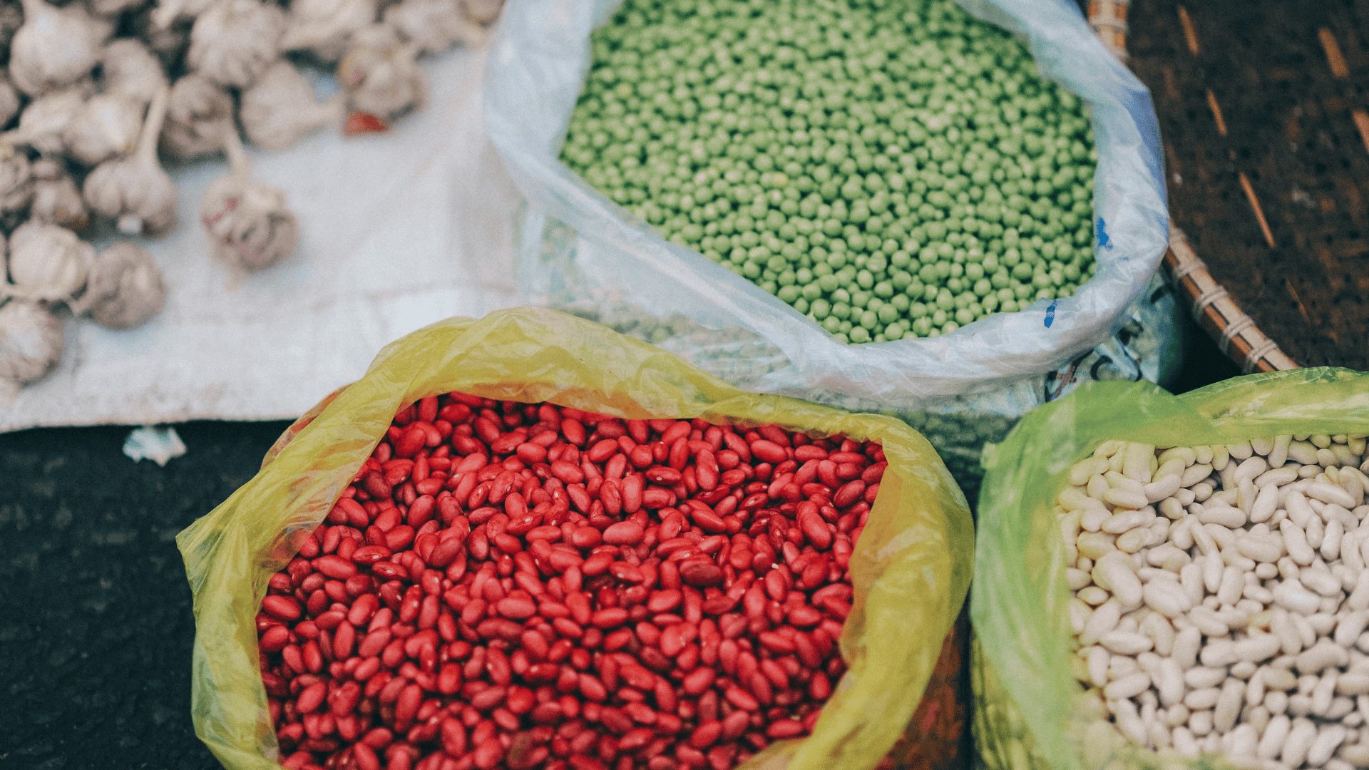 Closeup of colorful beans and garlic at a market stall.