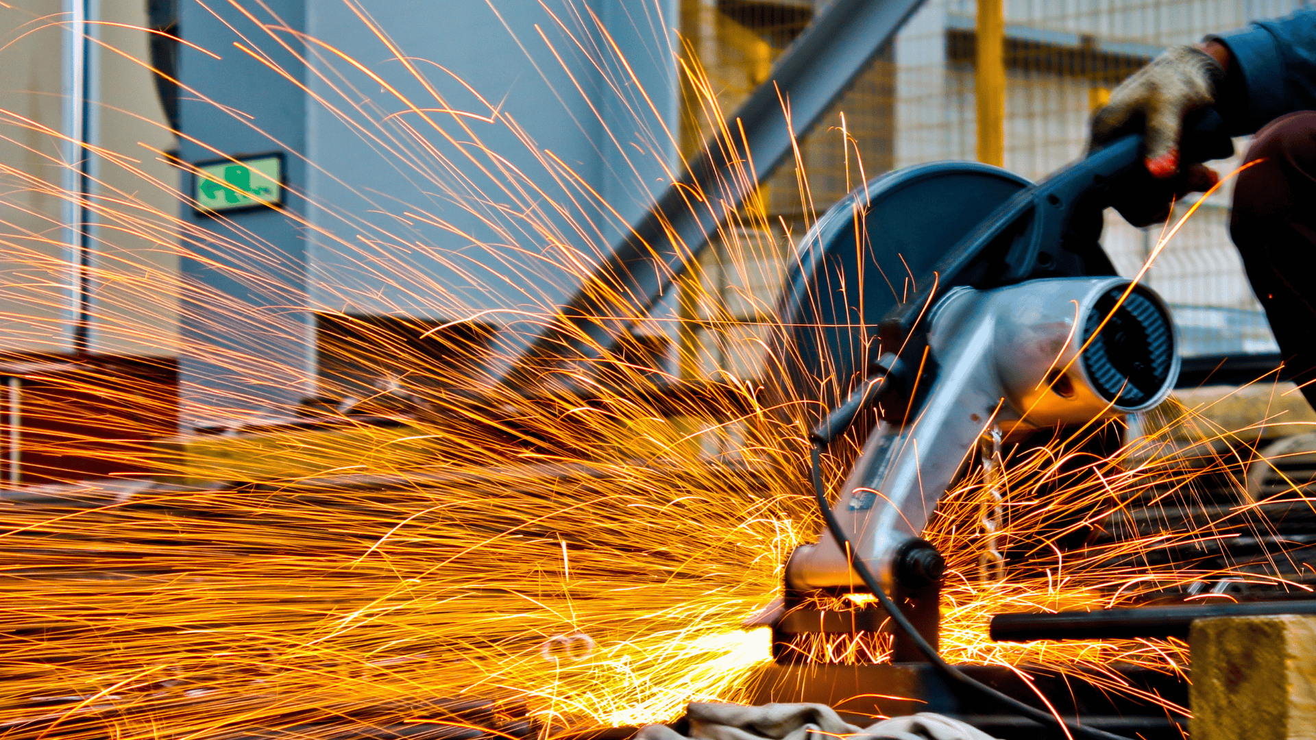 Worker using an angle grinder with bright sparks flying during metal cutting.