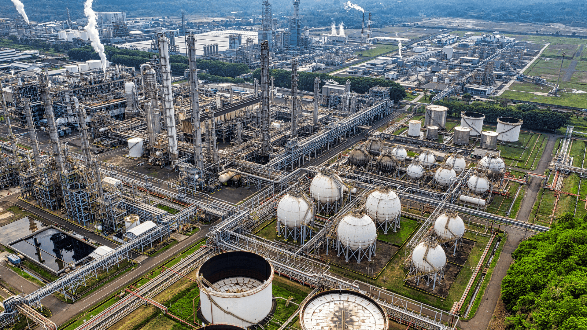 Aerial view of a large industrial oil and gas refinery complex with storage tanks and pipelines.
