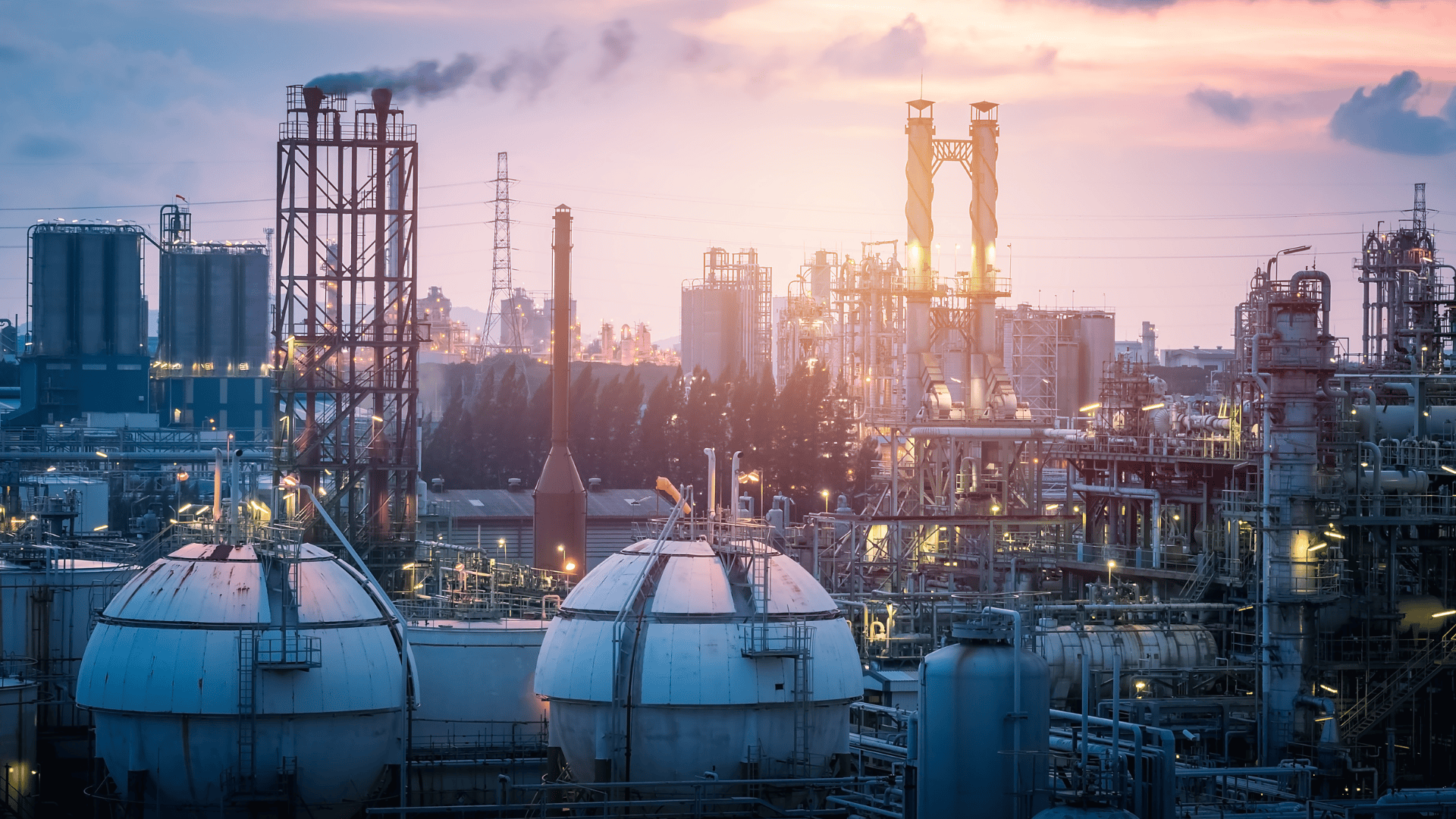 Large industrial refinery complex with storage tanks and towers at sunset.