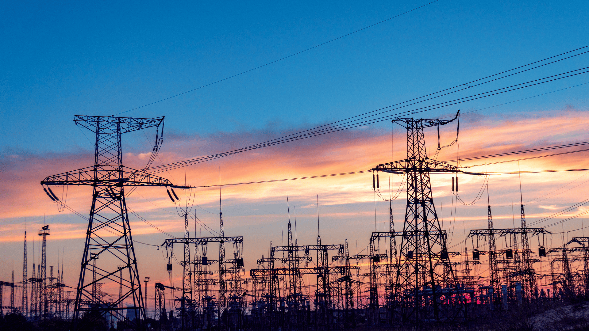 Power transmission towers silhouetted against a colorful sunset sky.