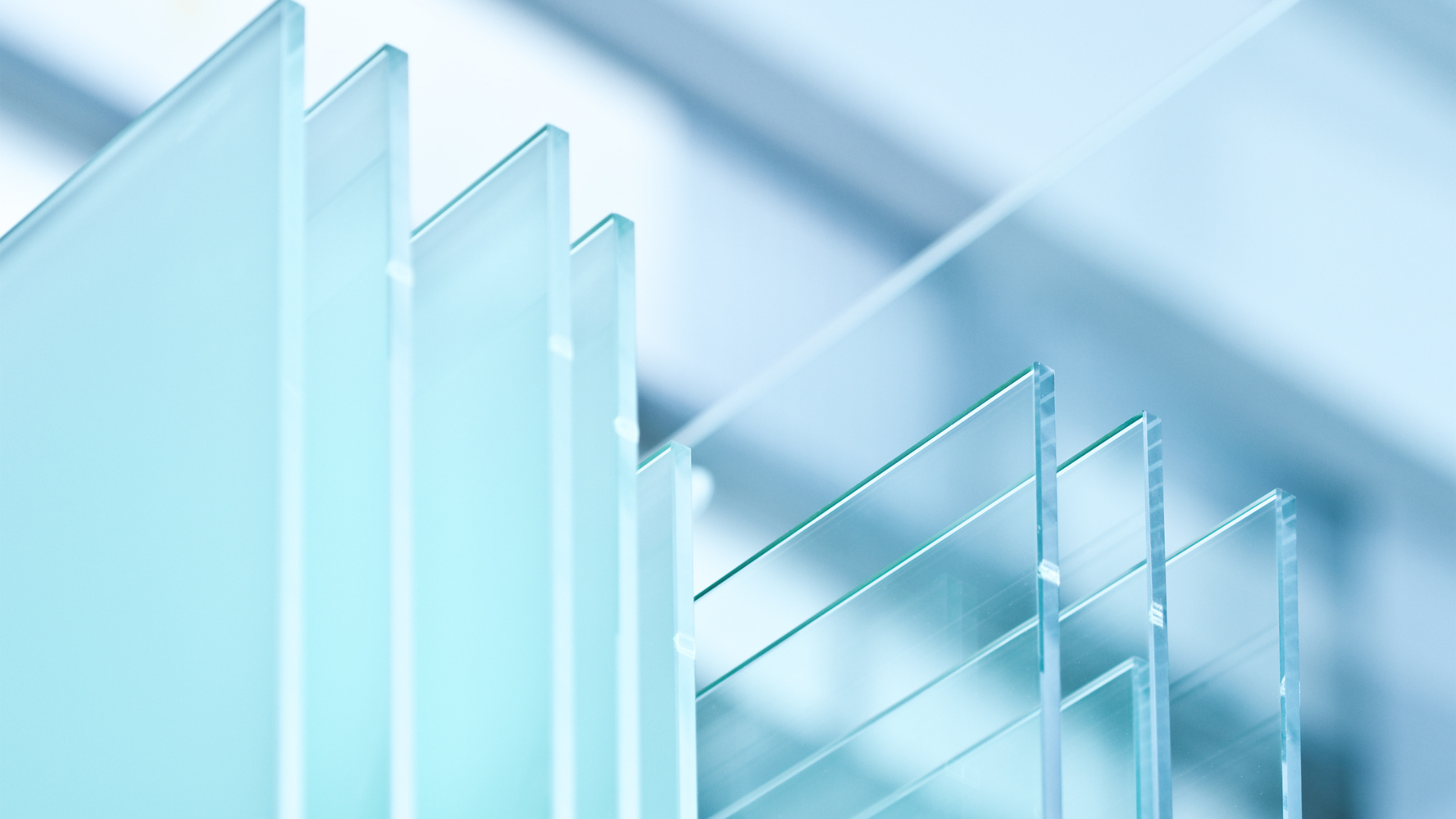 Sheets of transparent and frosted glass panels stacked in a modern industrial setting.