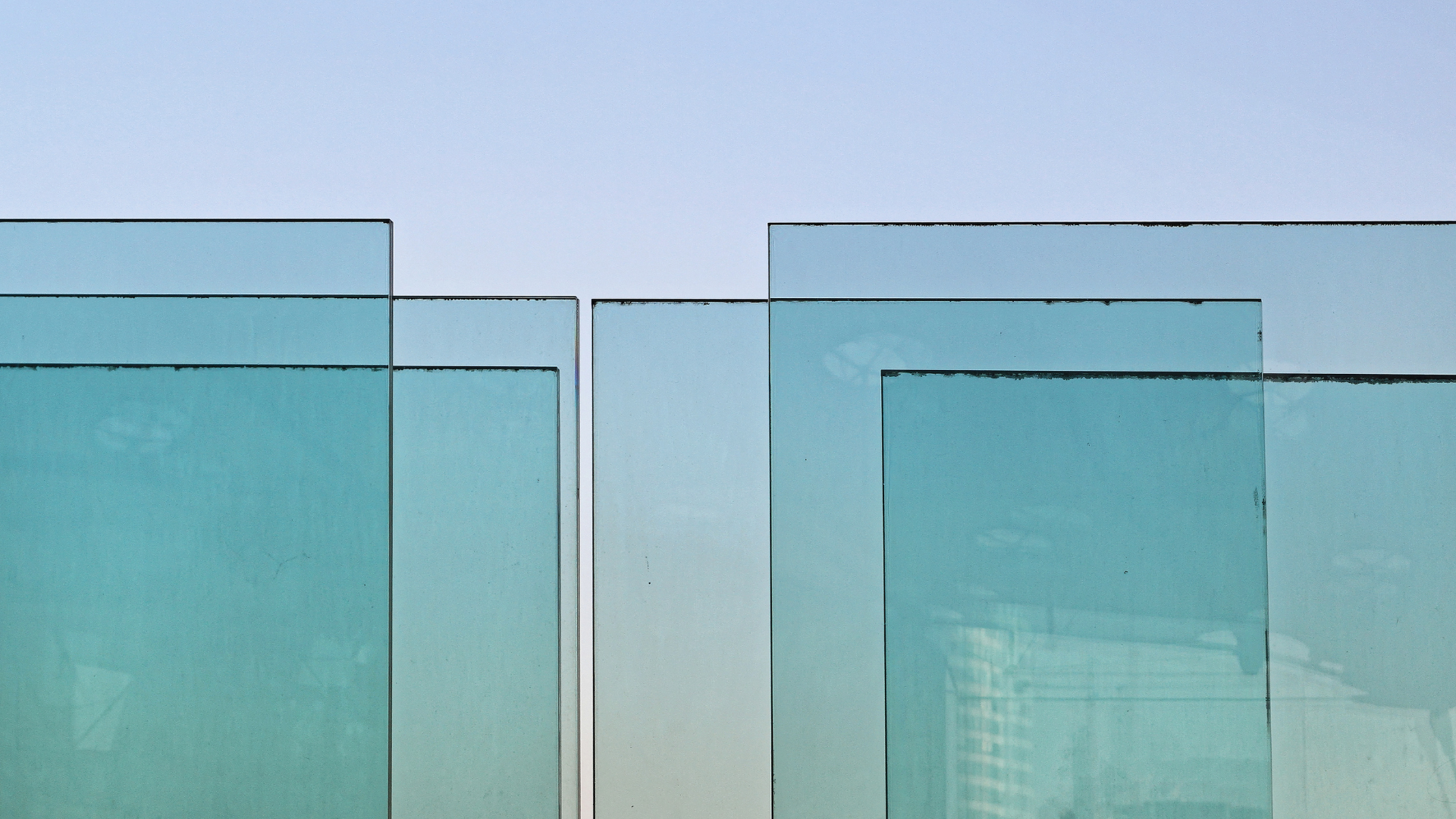 Overlapping blue-tinted glass panels stacked vertically against a clear sky.