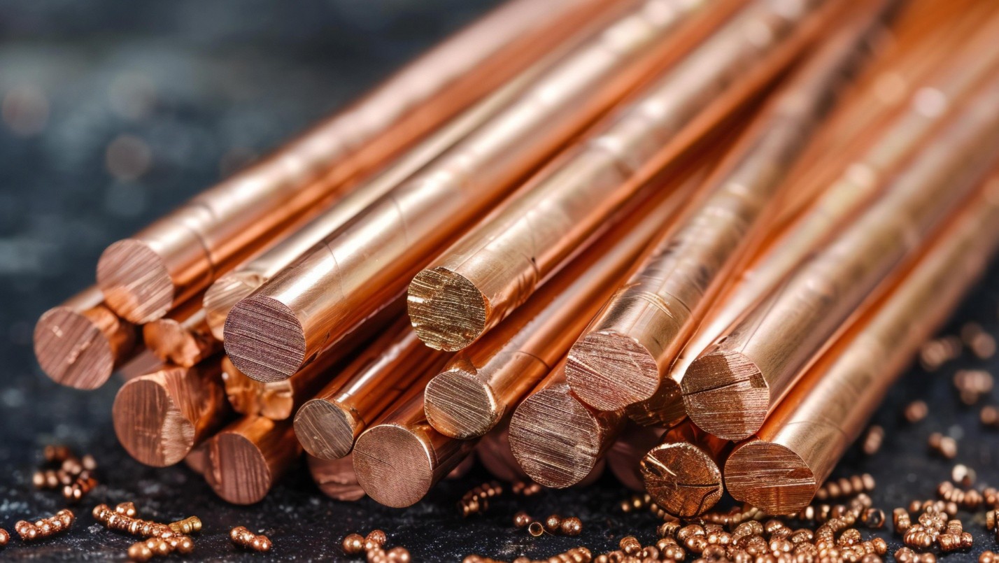 Stack of polished copper rods with small copper granules scattered around on a dark surface