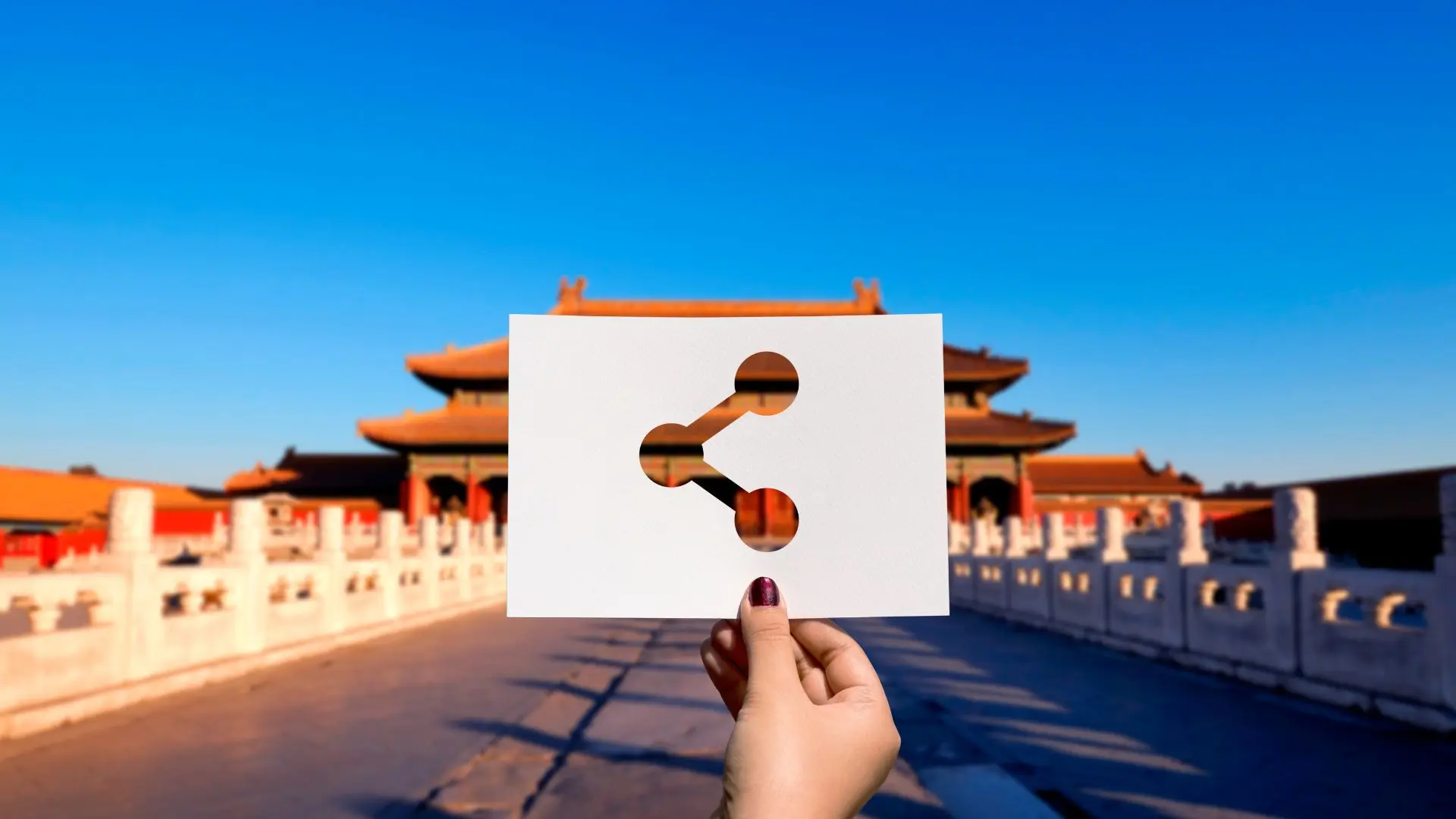 Hand holding a share icon card in front of the Forbidden City in Beijing, symbolising access to China’s financial and futures markets.