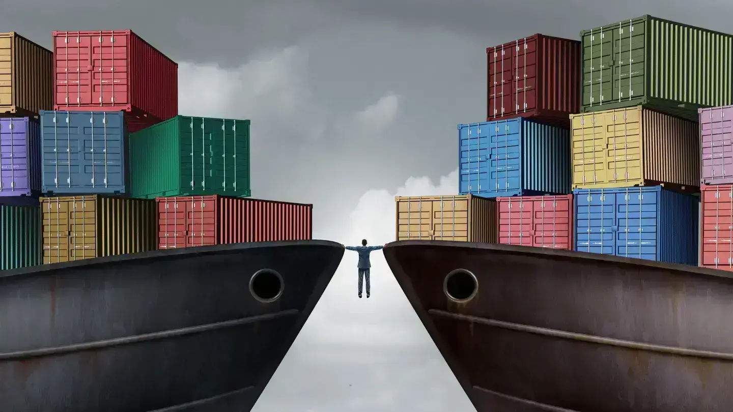 Shipping containers stacked on cargo ships facing each other with a person standing between them, symbolising global trade and trade balance tensions.